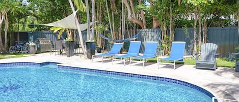 Una piscina con azulejos azules, rodeada de sillas de descanso y una hamaca.