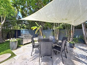 Une terrasse extérieure avec une table et des chaises, un barbecue et un espace ombragé.