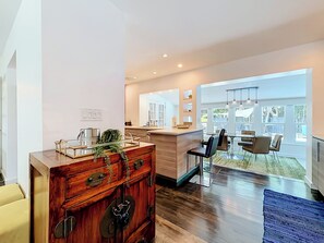 A modern kitchen with a wooden cabinet, a dining area with chairs, and a large window offering a view of the outdoors.