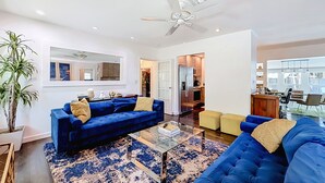 A modern living room with a blue sofa set, a glass coffee table, and a ceiling fan. - Modern Coastal Home Near Las Olas + Heated Pool (Fort Lauderdale)