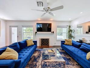 Un salon moderne avec deux canapés bleus, une cheminée, un téléviseur et un ventilateur de plafond.