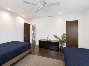 A hotel room with two beds, a ceiling fan, a small table, and a plant.