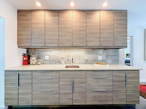A modern kitchen with wooden cabinets, a marble backsplash, and a built-in oven. - Modern Coastal Home Near Las Olas + Heated Pool (Fort Lauderdale)