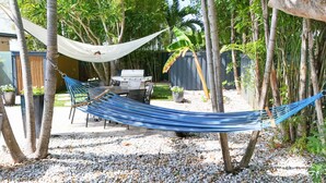 A hammock between trees in a backyard with a barbecue grill and potted plants. - Modern Coastal Home Near Las Olas + Heated Pool (Fort Lauderdale)