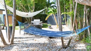 A hammock between trees in a backyard with a barbecue grill and potted plants. - Modern Coastal Home Near Las Olas + Heated Pool (Fort Lauderdale)