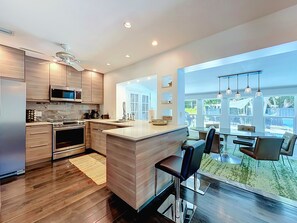 A modern kitchen with a central island, stainless steel appliances, and a view to a dining area with outdoor seating. - Modern Coastal Home Near Las Olas + Heated Pool (Fort Lauderdale)