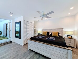 A bedroom with a bed, bedside tables, a ceiling fan, and a view through an open door. - Modern Coastal Home Near Las Olas + Heated Pool (Fort Lauderdale)