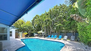 A swimming pool with a blue tiled edge, surrounded by a patio with stone tiles and a blue awning. - Modern Coastal Home Near Las Olas + Heated Pool (Fort Lauderdale)