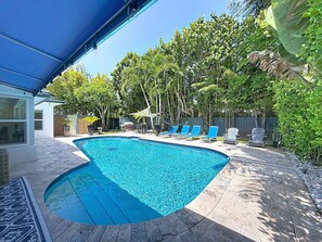 A swimming pool with a blue tiled edge, surrounded by a patio with stone tiles and a blue awning. - Modern Coastal Home Near Las Olas + Heated Pool (Fort Lauderdale)