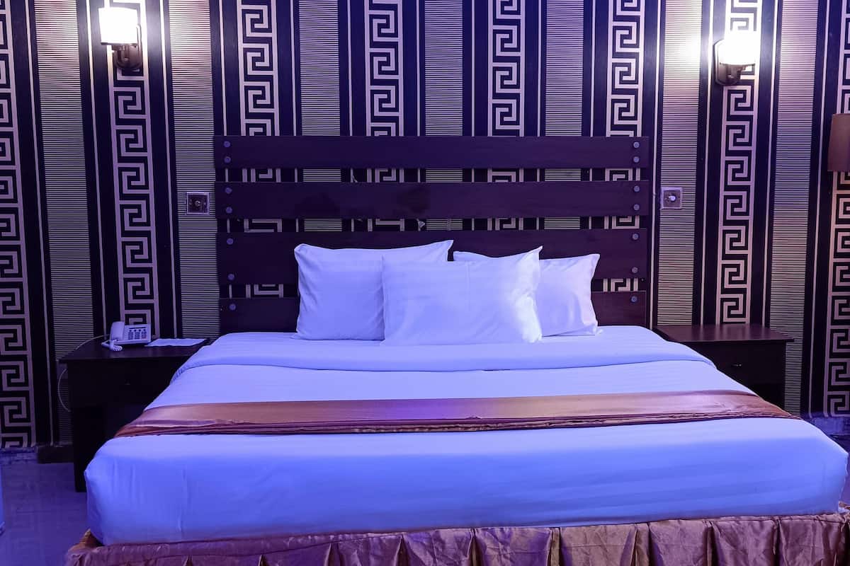 Hotelkamer met een groot bed, twee nachtkastjes, een wand met een geometrisch patroon en een lamp.