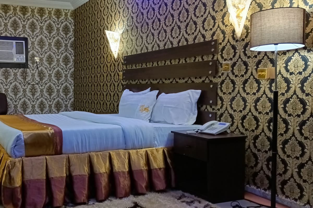 Een hotelkamer met een bed, een bureau, een stoel, een lamp en een wandairconditioner.
