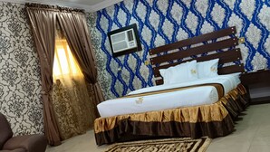 Une chambre à coucher avec un lit, des rideaux, un climatiseur fixé au mur et un papier peint à motifs.