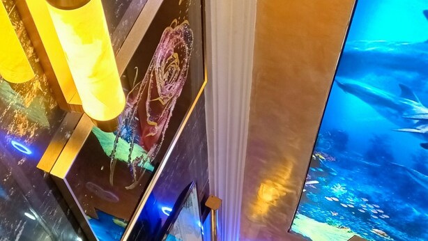 Un intérieur moderne avec un plafond haut, un éclairage encastré et un grand écran numérique affichant un paysage pittoresque.