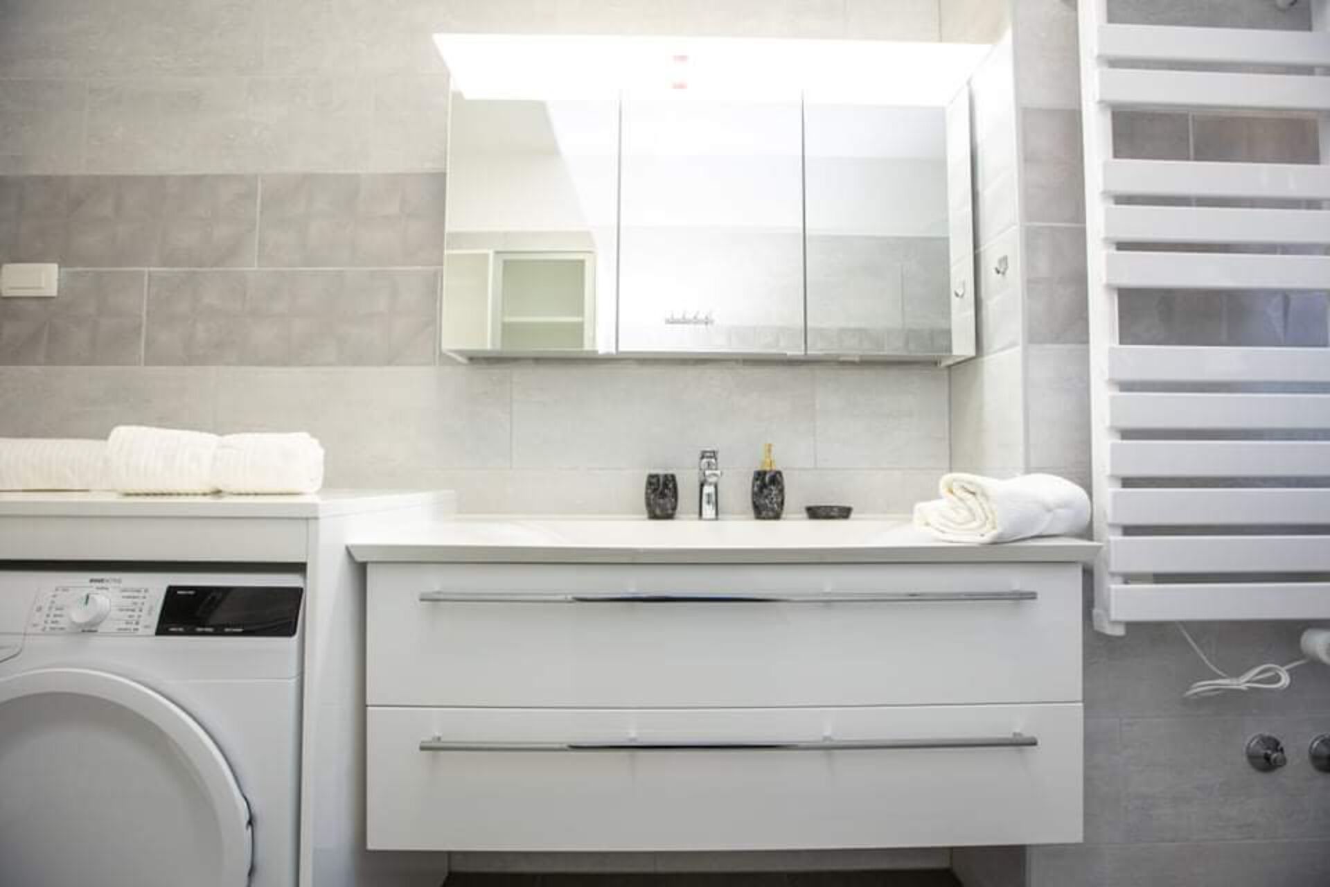 Un baño moderno con lavamanos blanco, espejo e lavadora integrada.