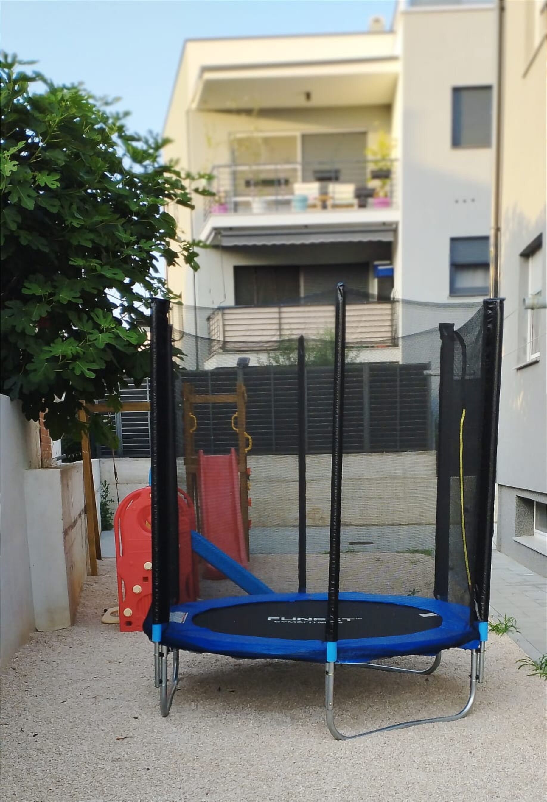 Un trampolín en un área exterior cercada, con un edificio al fondo.