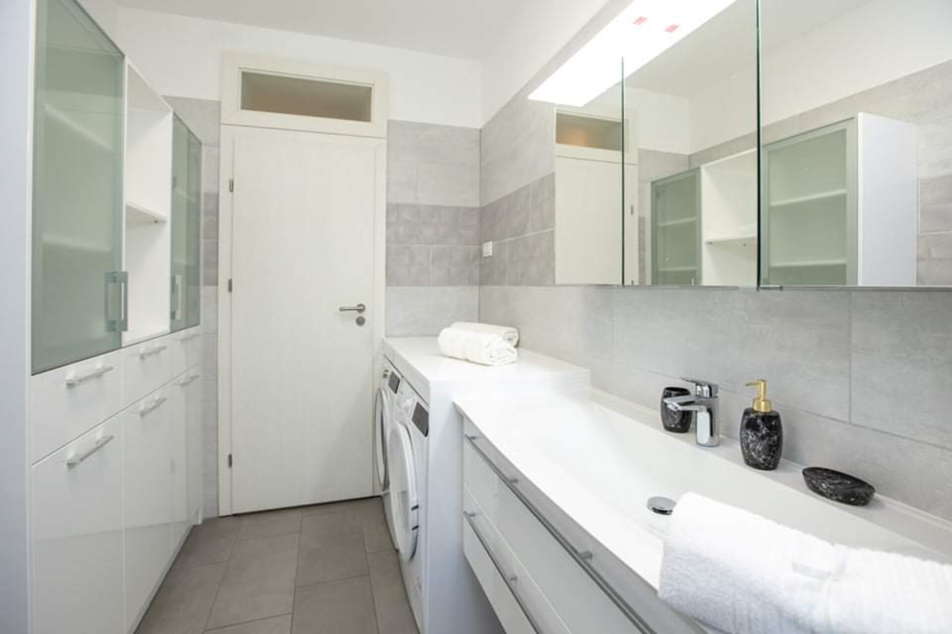 A modern bathroom with a white sink, a mirror, a towel, and a bottle of soap.