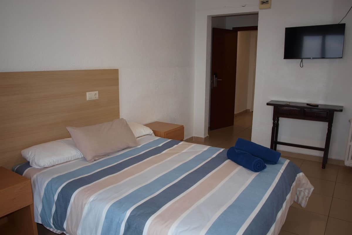 Een hotelkamer met een bed, nachtkastje, houten hoofdbord, een aan de muur bevestigde televisie en een kleine tafel.