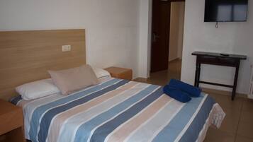 Habitación de hotel con una cama, una mesita de noche, un cabecero de madera, un televisor montado en la pared y una pequeña mesa.