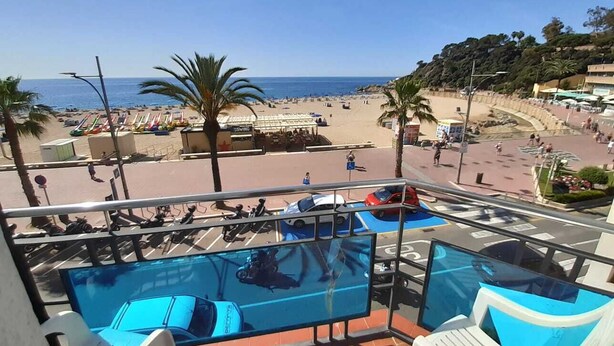 A balcony with a pool, beach view, palm trees, and a parking area.