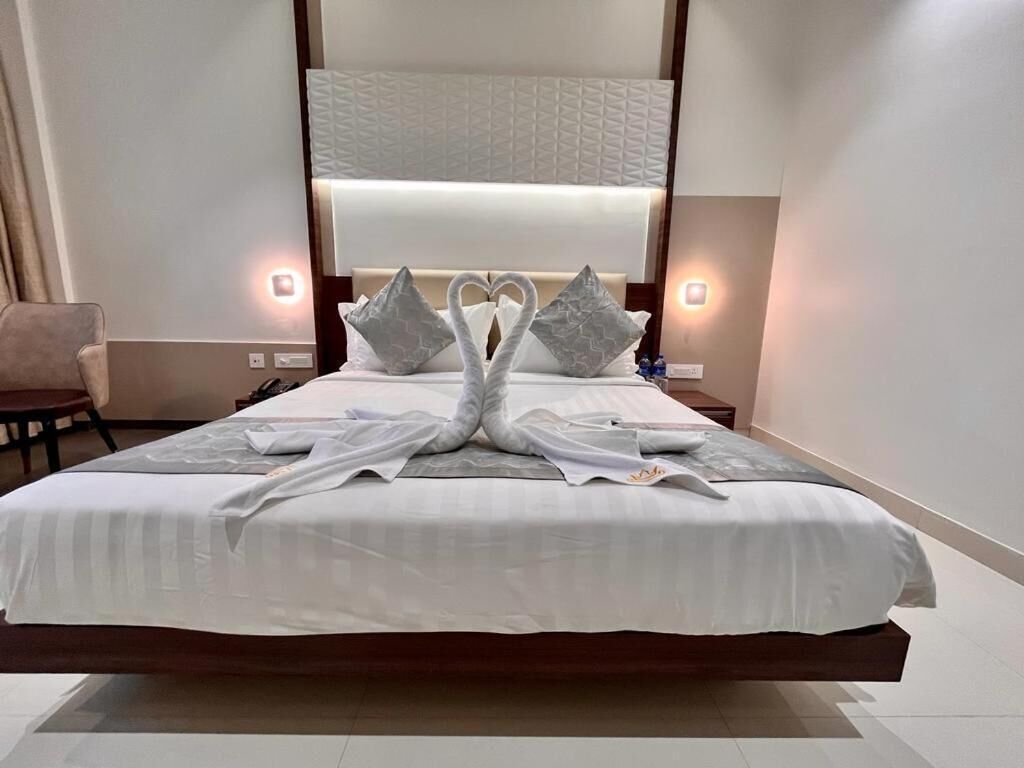 A hotel room with a large bed, two bedside lamps, a chair, and a wall-mounted light fixture.