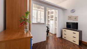 Una sala de estar moderna con un mueble de madera, un jarrón con flores, un televisor sobre un mueble y vistas hacia un comedor.