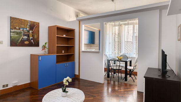 Una sala de estar moderna con un aparador de madera, una mesa de mimbre blanca con un jarrón y una zona de comedor con sillas y una mesa.
