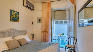 Un dormitorio con cama, una silla, un balcón con mesa y sillas, y una ventana con cortinas.
