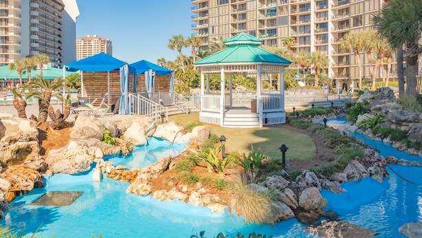Un espace piscine aménagé dans un complexe hôtelier, comprenant un kiosque, des chaises longues et un élément décoratif aquatique.
