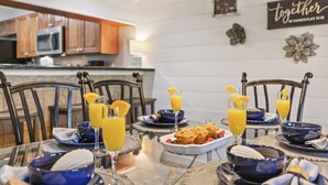 Un coin repas avec une table dressée pour quatre personnes, agrémentée d’une vaisselle bleue et blanche, de verres de jus d’orange et d’une assiette de muffins.