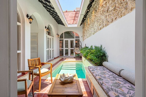 Un patio luminoso con piscina, mobiliario y una pared de piedra.