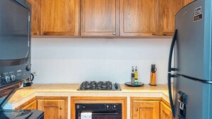 Eine kleine Küche mit Holzschränken, einem Gasherd, einem Backofen und einem Kühlschrank.