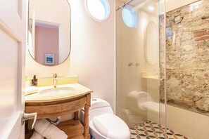 Un baño con tocador de madera, inodoro y ducha con mampara de vidrio y pared de piedra.