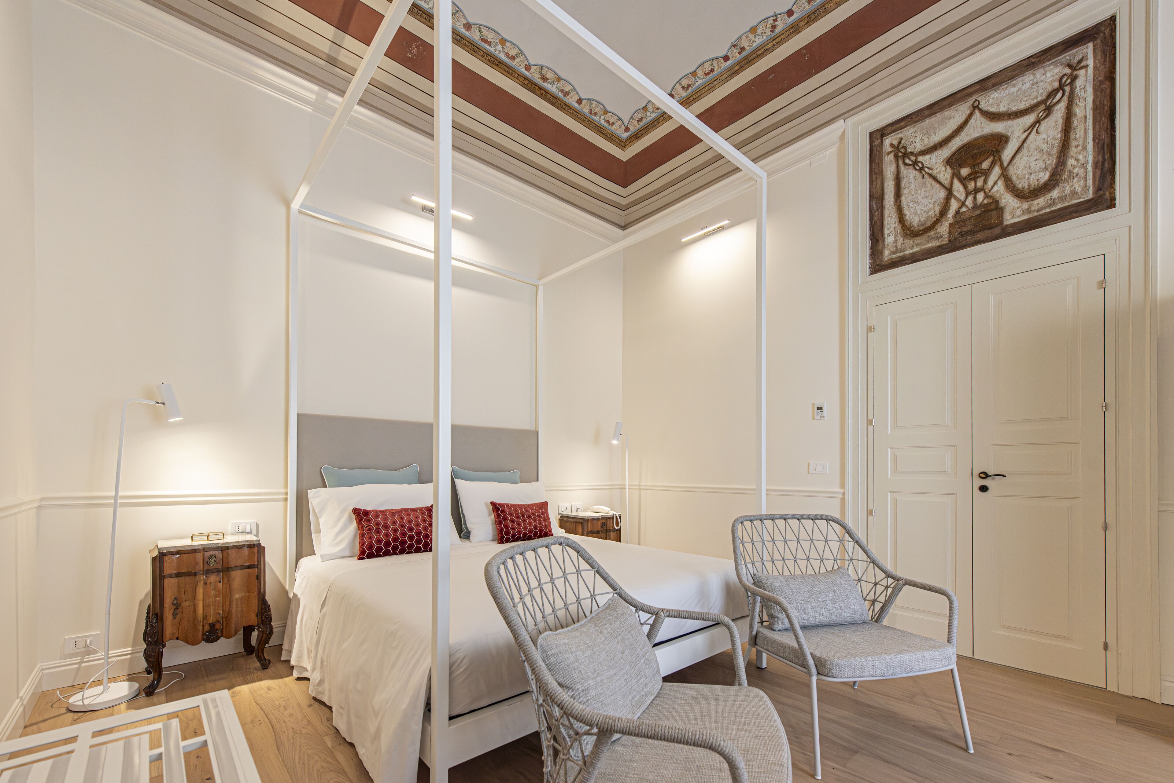 A bedroom with a four-poster bed, two wicker chairs, a bedside table, and a nightstand.