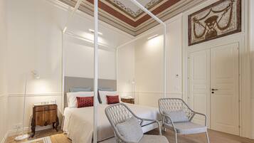 A bedroom with a four-poster bed, two wicker chairs, a bedside table, and a nightstand.