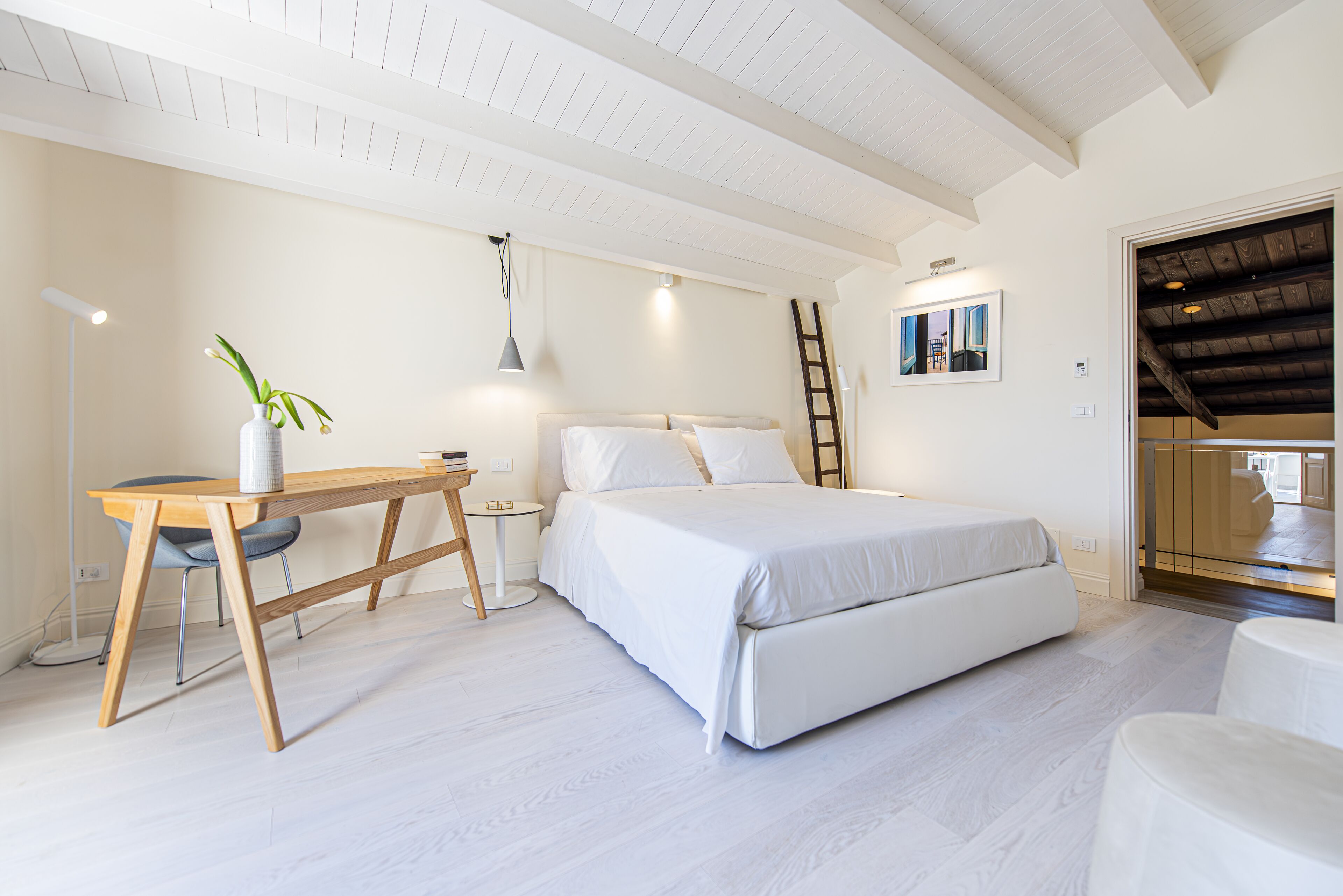 A bedroom with a bed, a desk, a chair, a ladder, and a small table.