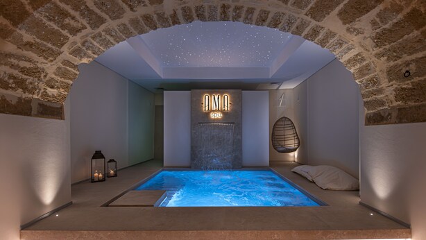 Un cuarto de spa con pared de piedra, un letrero que dice "AMA Spa", una piscina pequeña y dos faroles.