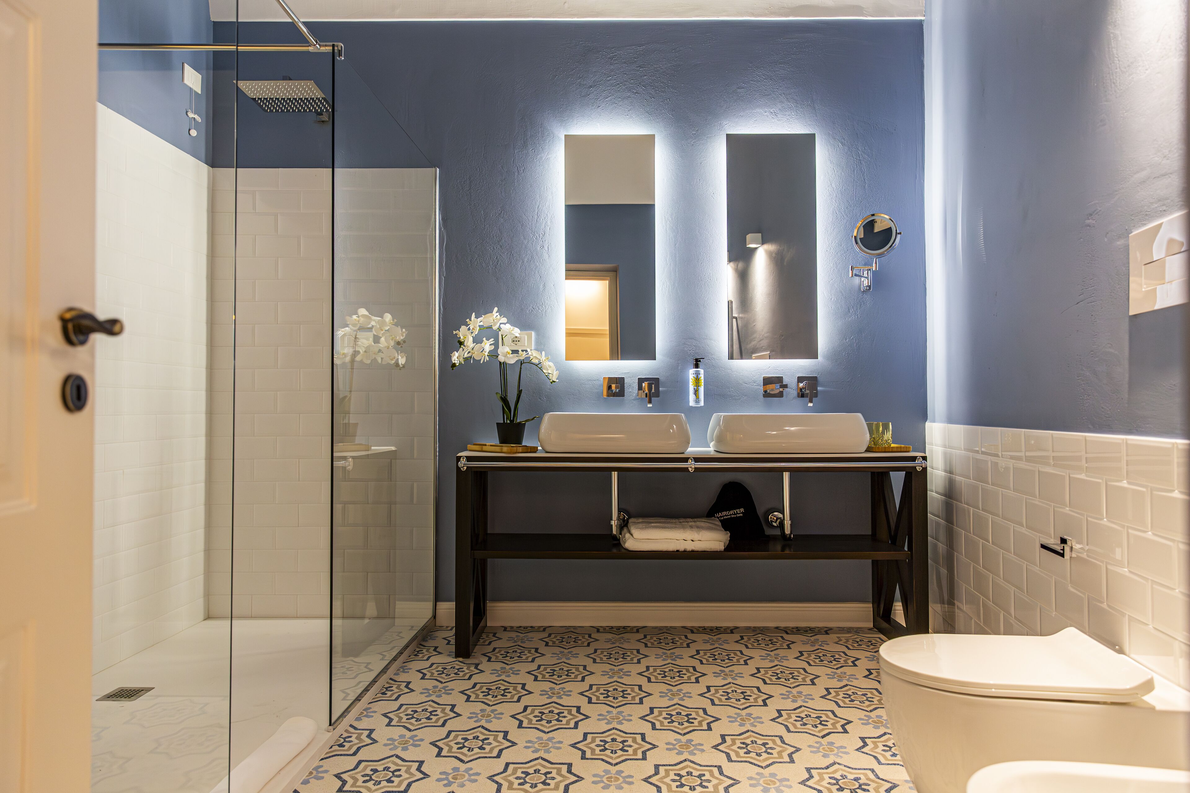A bathroom with a glass shower enclosure, a sink vanity with two mirrors, and a patterned floor.