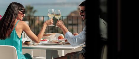 A couple toasting with wine glasses at a table with a view of the sea.