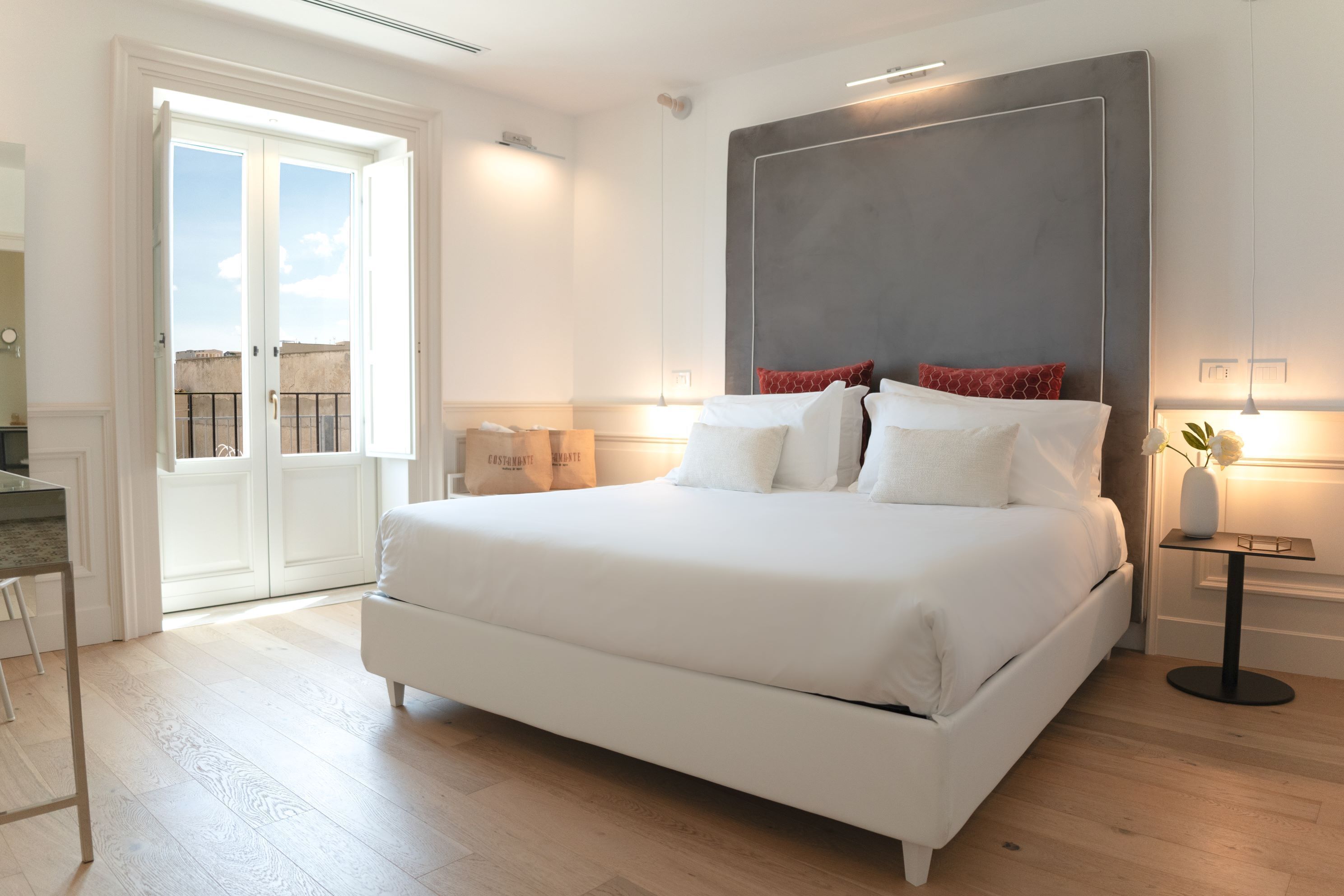 A modern bedroom with a large bed, a bedside table, a chair, and a view of the outside balcony.
