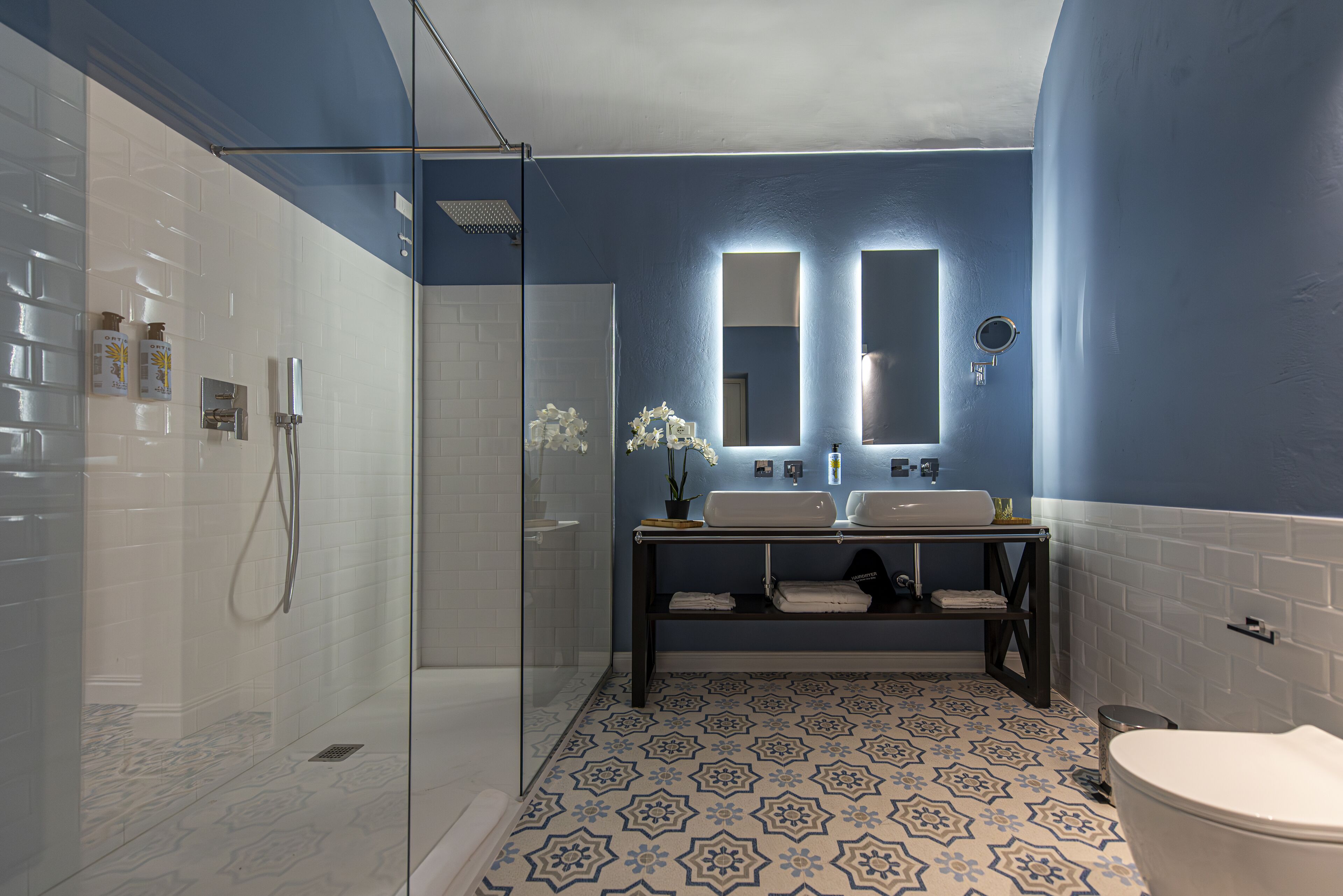 Une salle de bain avec une douche à parois de verre, deux lavabos, des toilettes et des carreaux de sol à motifs.