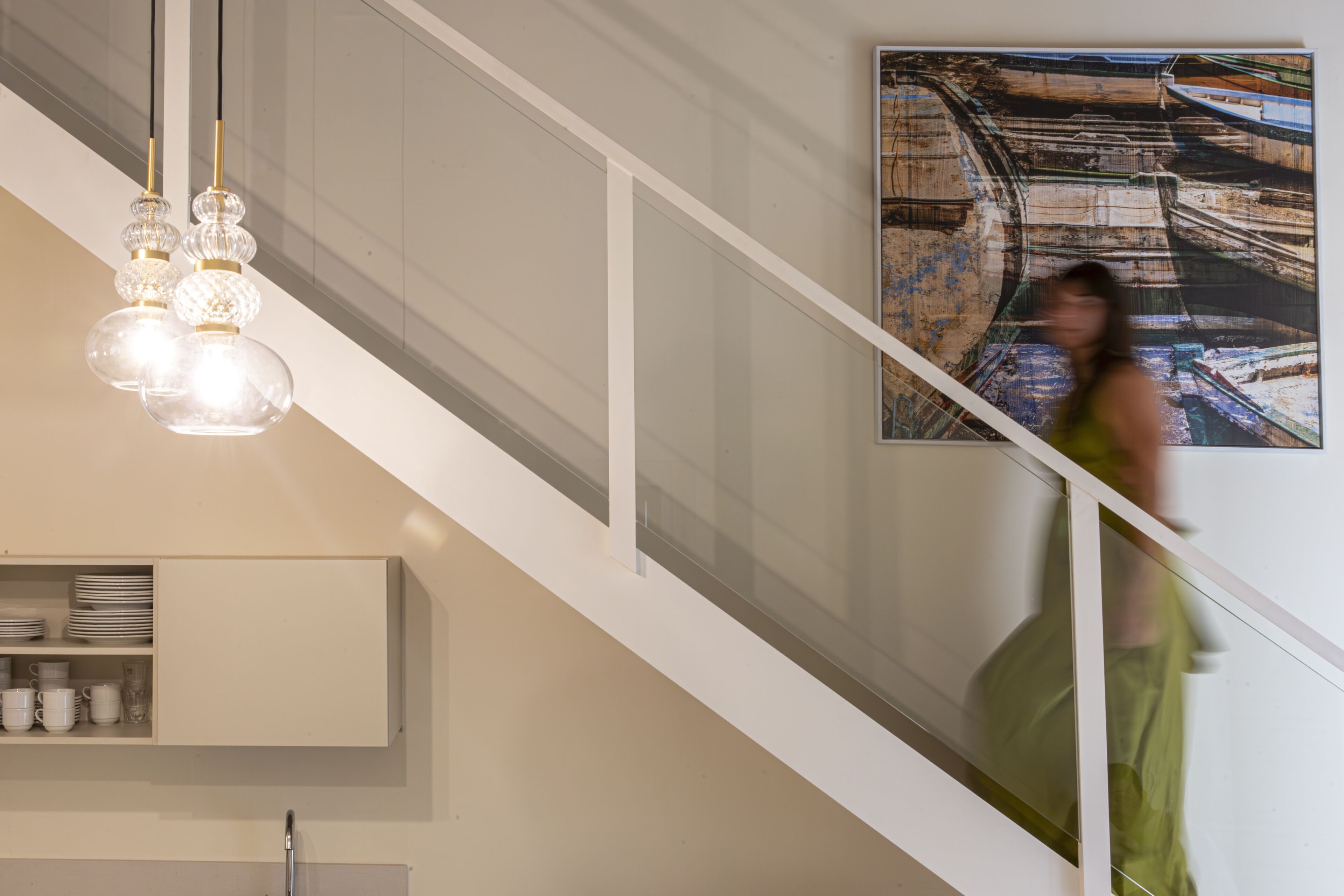 A staircase with a modern design, a hanging light fixture, and a wall-mounted shelf with dishes.