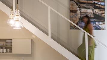 A staircase with a modern design, a hanging light fixture, and a wall-mounted shelf with dishes.