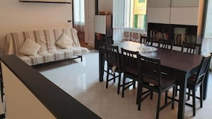 Un salon comprenant un canapé, une table à manger avec des chaises, une bibliothèque et une fenêtre avec des rideaux.