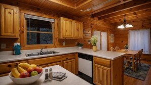 Interno di una baita in legno con angolo cottura e sala da pranzo, pensili in legno, lavello, lavastoviglie e tavolo con sedie.