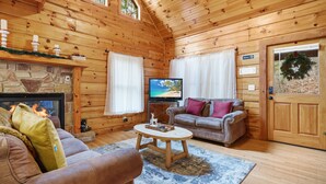 Un accogliente interno di una baita in legno con camino in pietra, televisione e zona salotto confortevole.