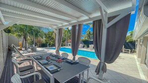 An outdoor dining area with a pool view, covered patio, and poolside chairs.