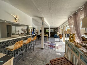 Cozinha espaçosa com bancada de mármore, banquetas de bar e área de jantar com tapete estampado.