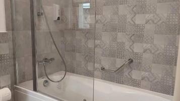 Uma casa de banho moderna com cabine de duche em vidro, banheira branca e azulejos estampados nas paredes.