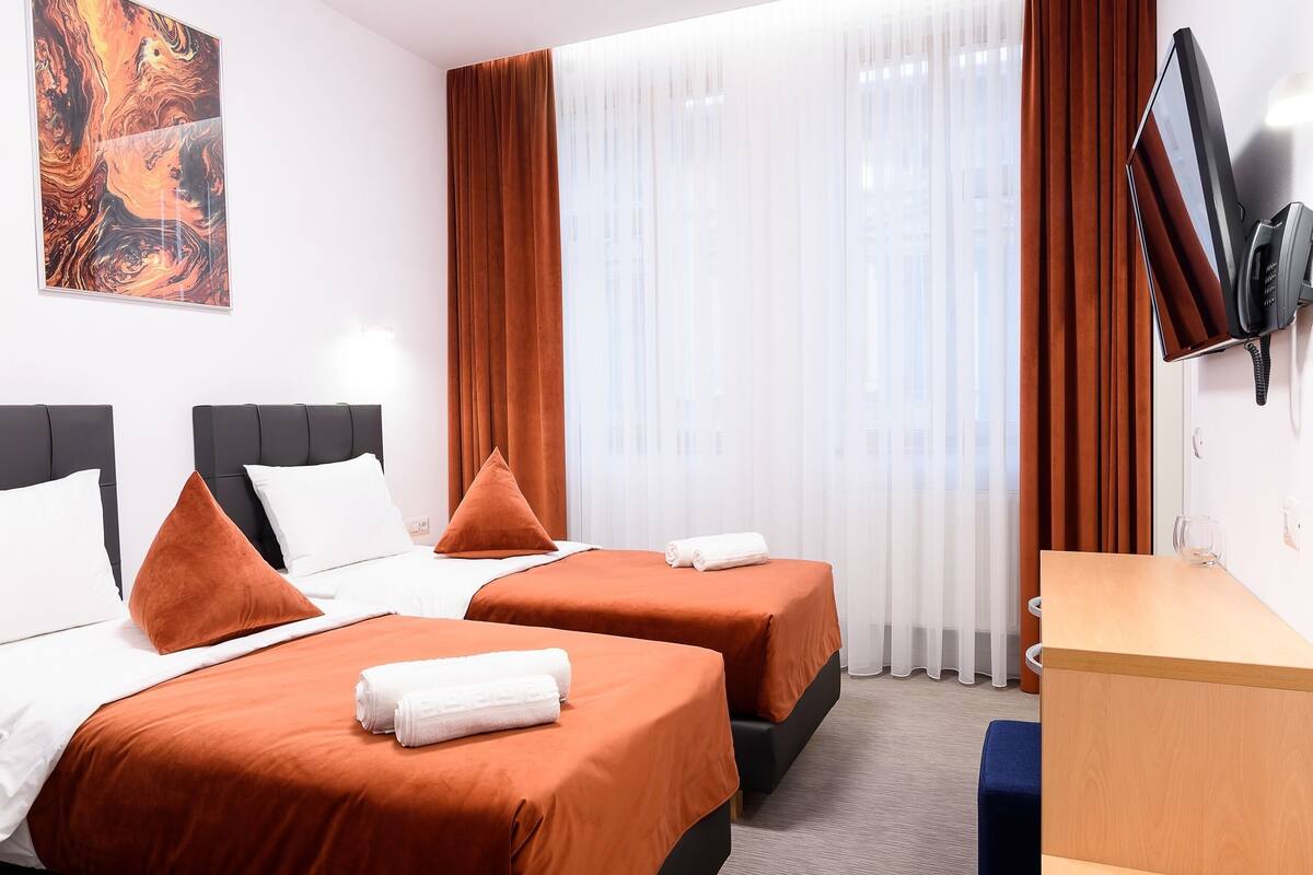 A hotel room with two beds, a desk, a TV, and a painting on the wall.
