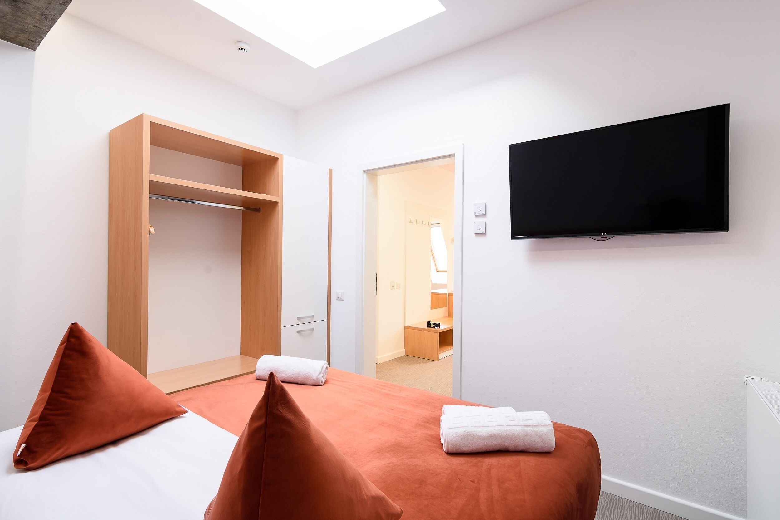 Habitación de hotel con cama, armario, televisor y baño visible a través de una puerta abierta.